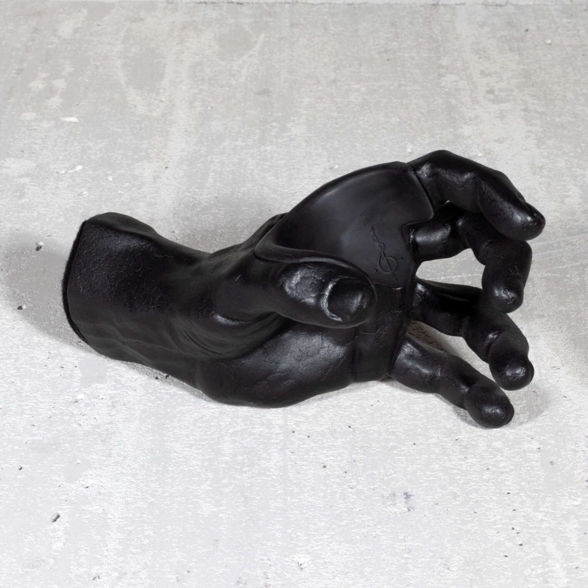 Black cast hand sculpture instrument hanger on a gray concrete surface.
