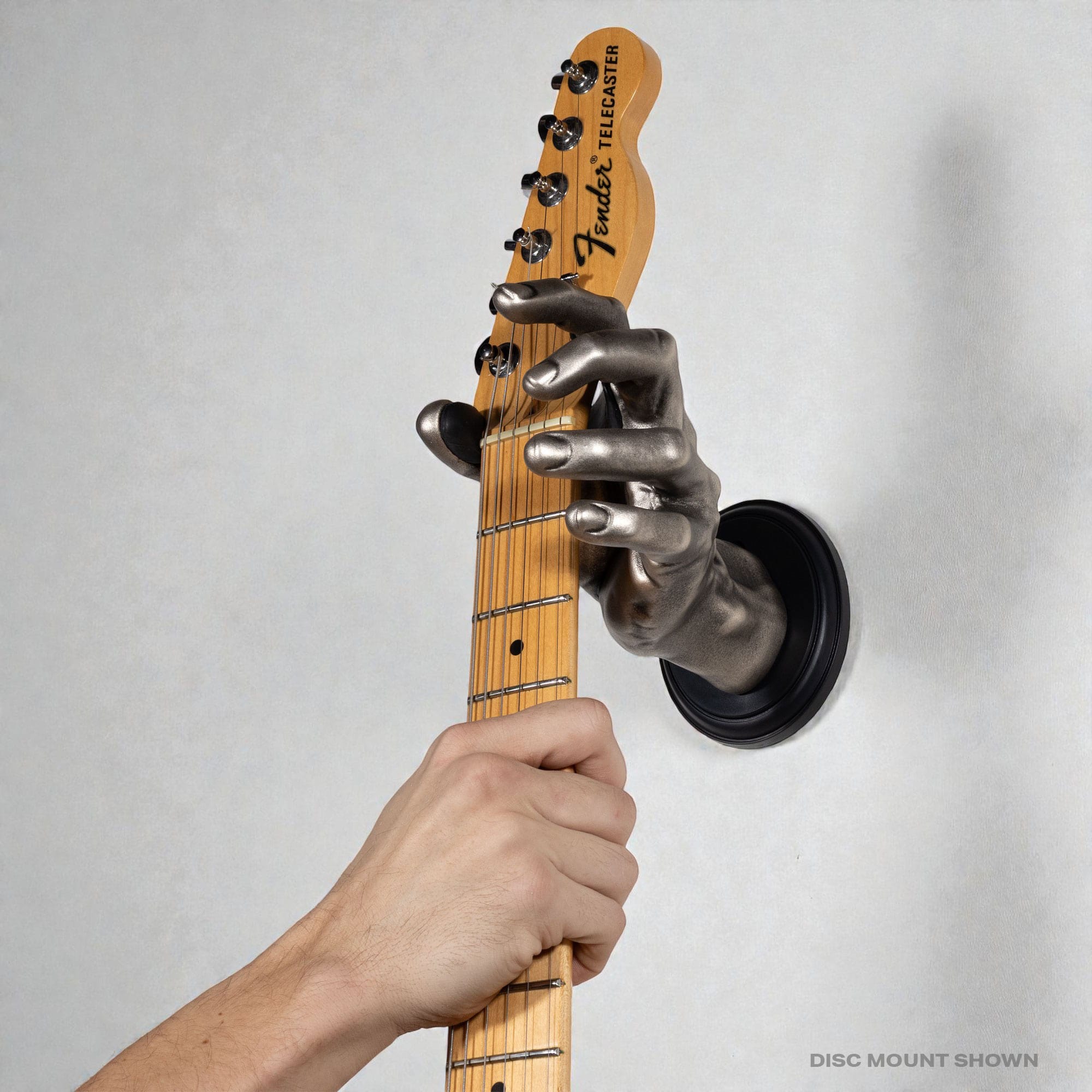 GuitarGrip silver male hand holding a telecaster guitar on the wall.