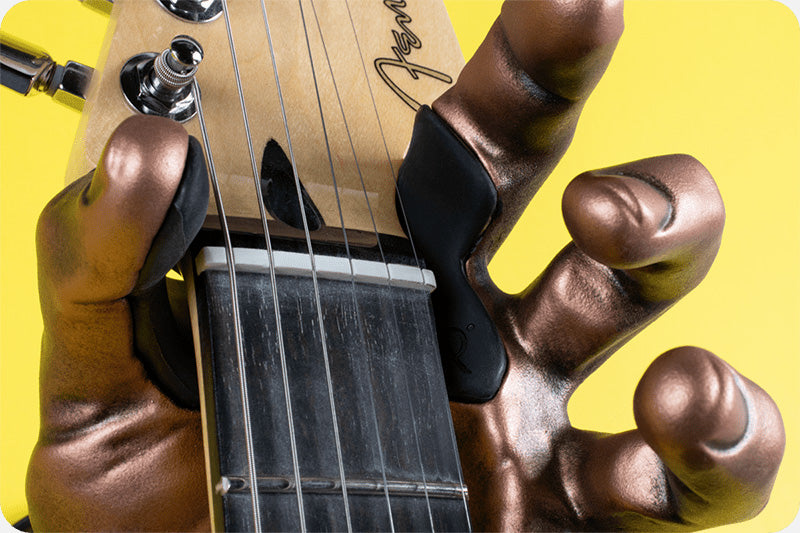 Copper hand guitar hook wall mount on yellow background holding fender guitar. 