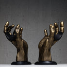 Two bronze hand sculpture guitar hangers on black bases against a gray background.

