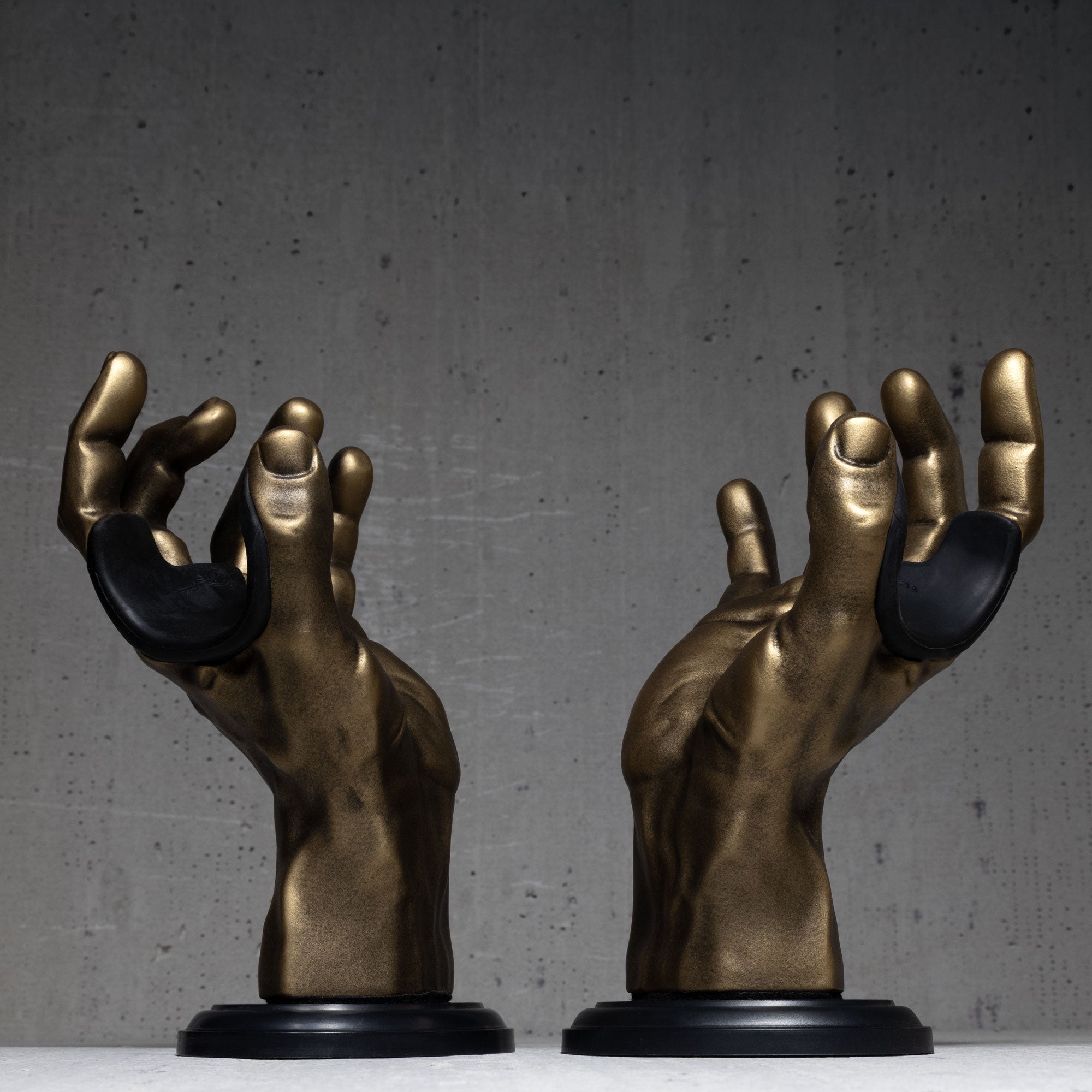 Two bronze hand sculpture guitar hangers on black bases against a gray background.

