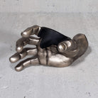 Metallic hand sculpture guitar hanger on a gray surface.

