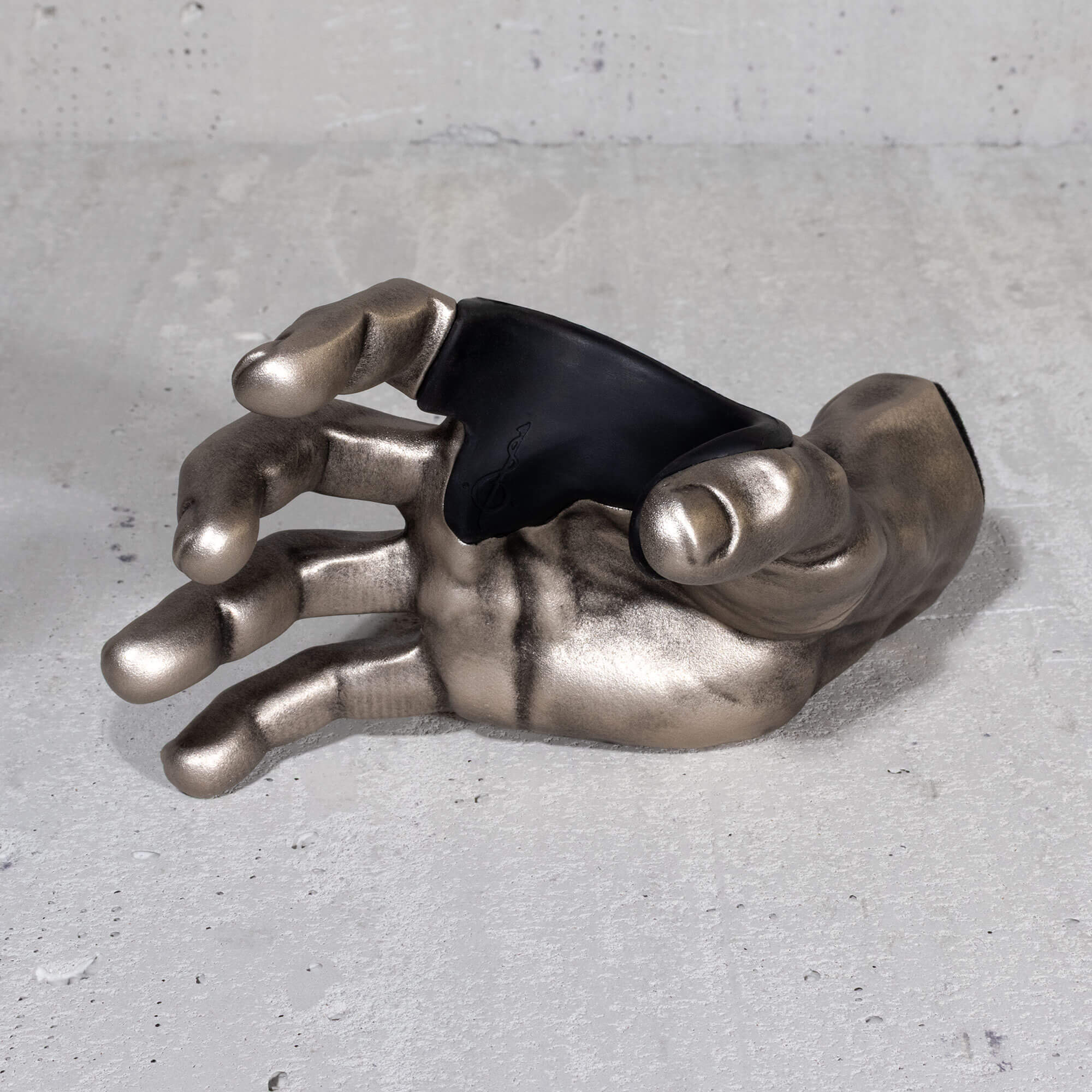 Metallic hand sculpture guitar hanger on a gray surface.

