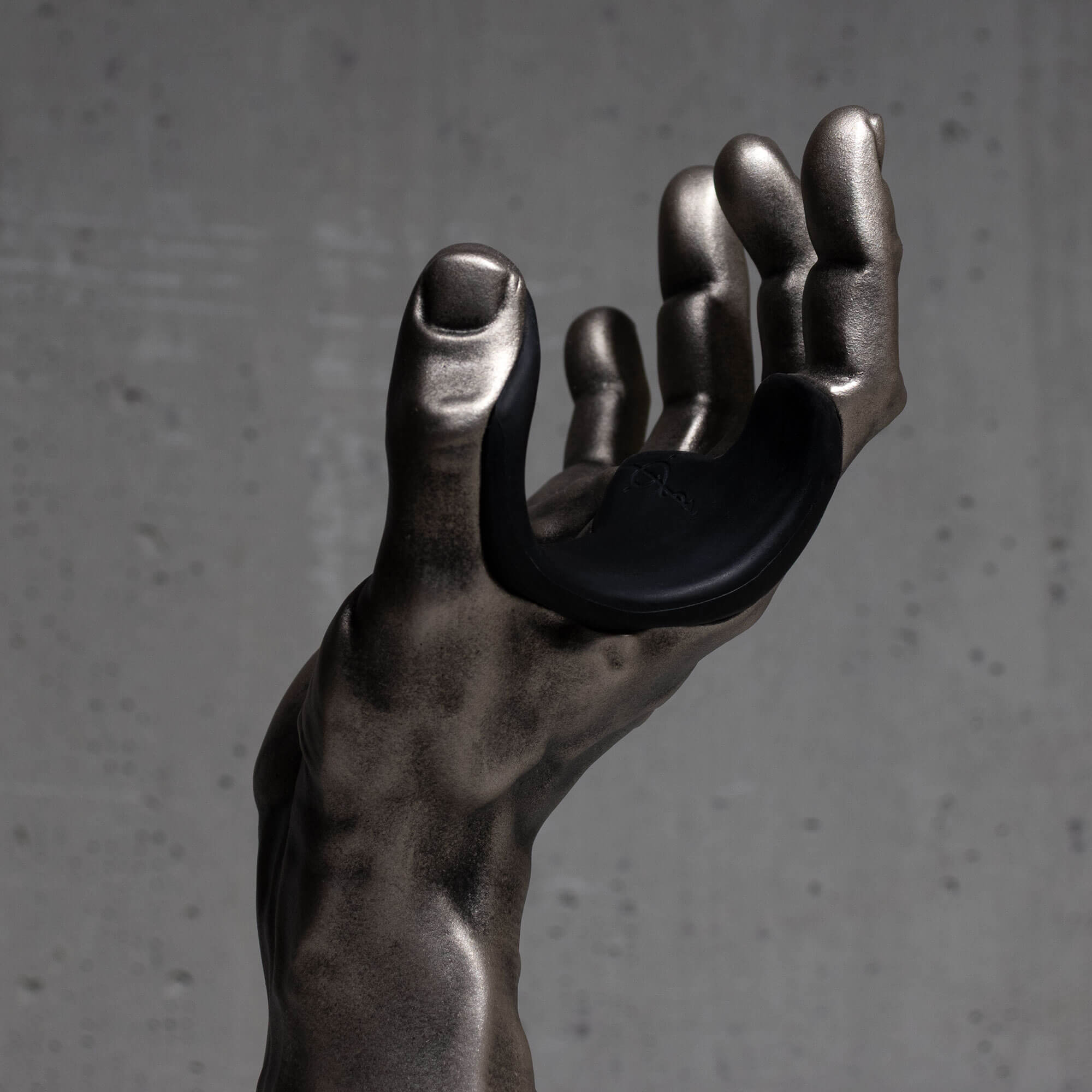 Silver hand guitar hanger wall mount sculpture against a gray background.

